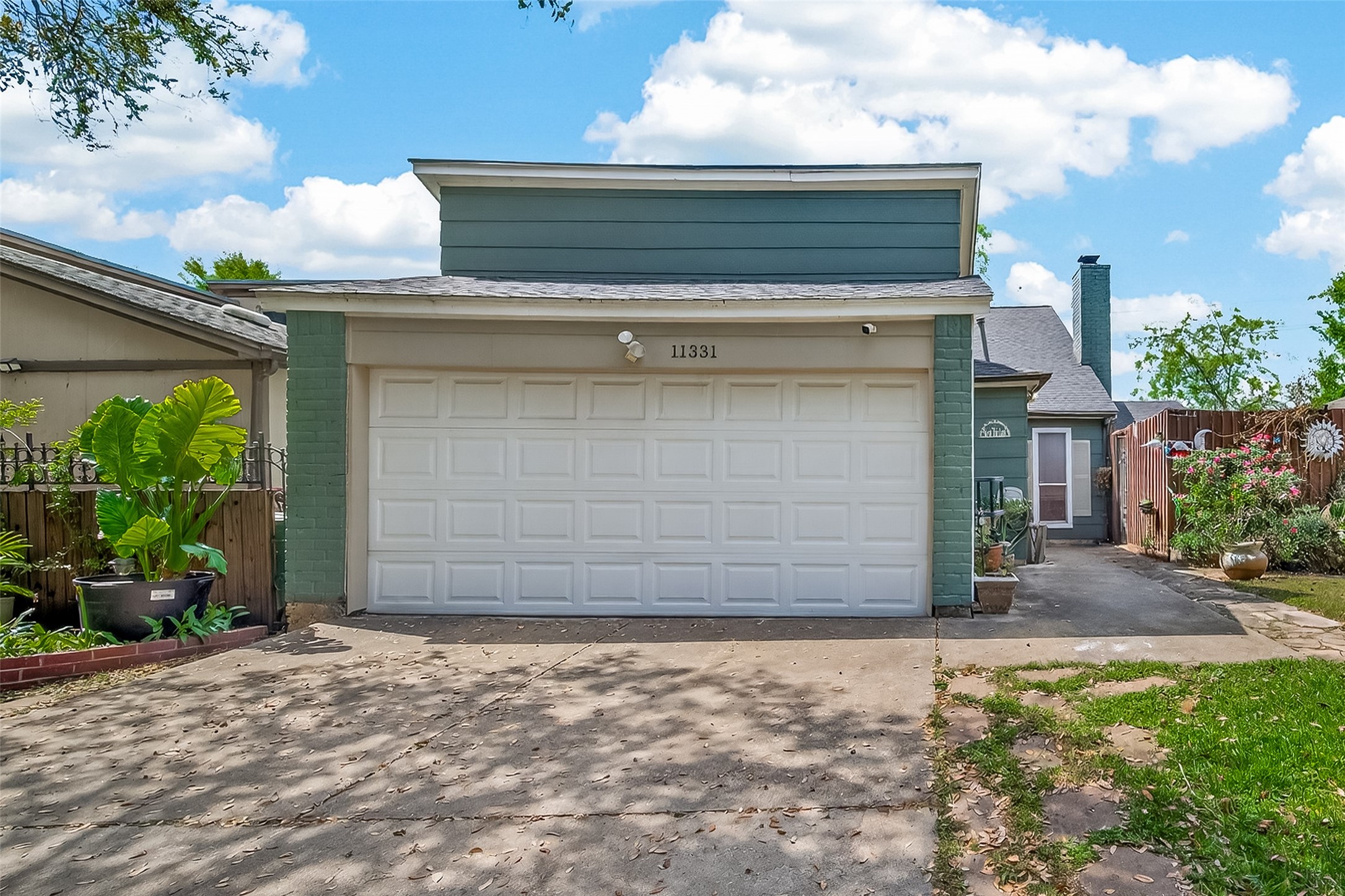 11331 Oakcenter Drive Houston, TX 77072 - Photo 2 of 35 This home features a modern exterior with a two-car garage, light blue-green siding, and a well-maintained driveway. It has a charming front garden with lush plants and a cozy, private entrance pathway.