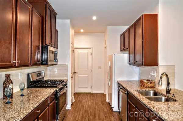 a kitchen with stainless steel appliances granite countertop a refrigerator a stove and a sink with wooden cabinets