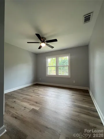 an empty room with wooden floor fan and windows