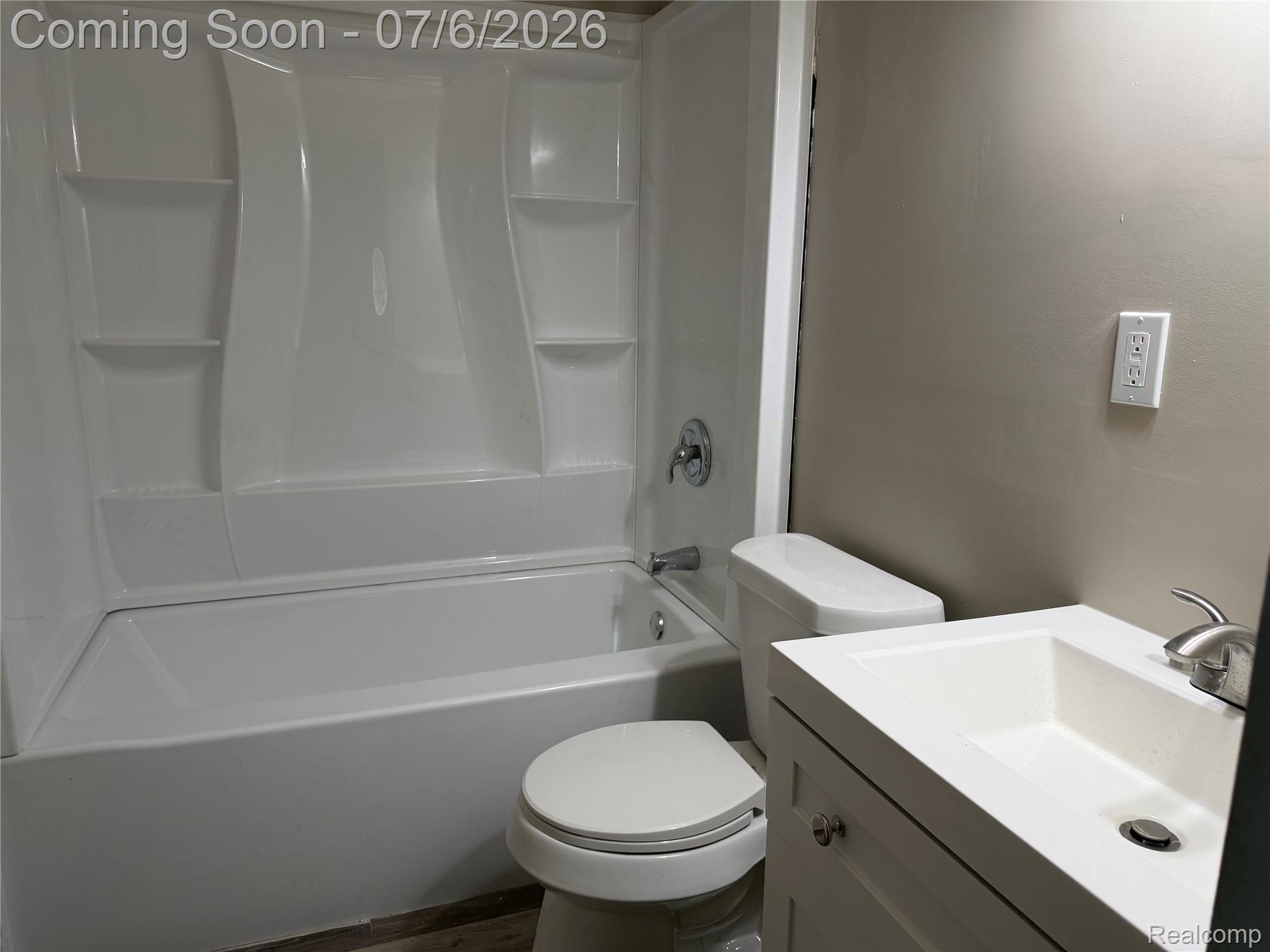 808 Division Street Owosso, MI 48867 - Photo 12 of 25 Bathroom featuring a white bathtub with an integrated shower surround, built-in shelving, a white toilet, and a white vanity with an integrated sink and brushed nickel faucet