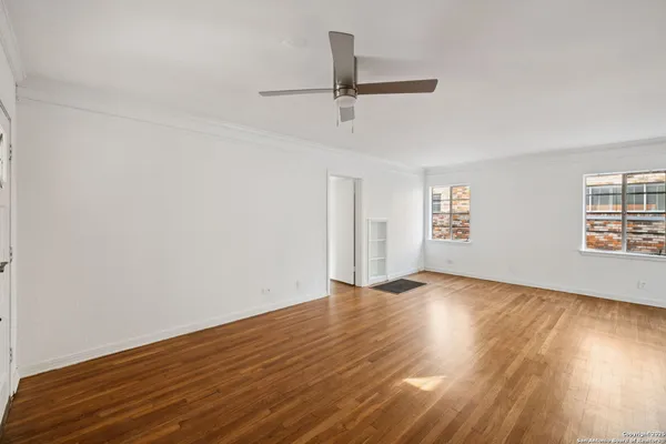 an empty room with wooden floor fan and windows