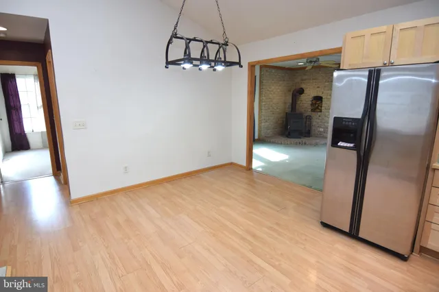 a view of a refrigerator in kitchen and an empty room with wooden floor and windows