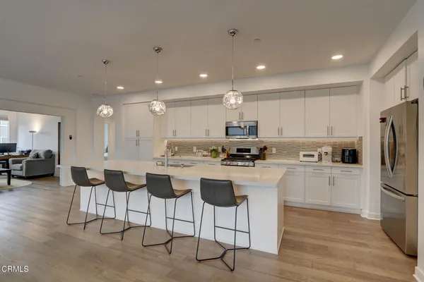 a kitchen with stainless steel appliances kitchen island granite countertop a stove a refrigerator a kitchen island with couches chairs and wooden floor