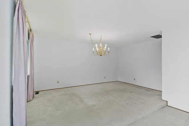 an empty room with chandelier fan and wooden floor