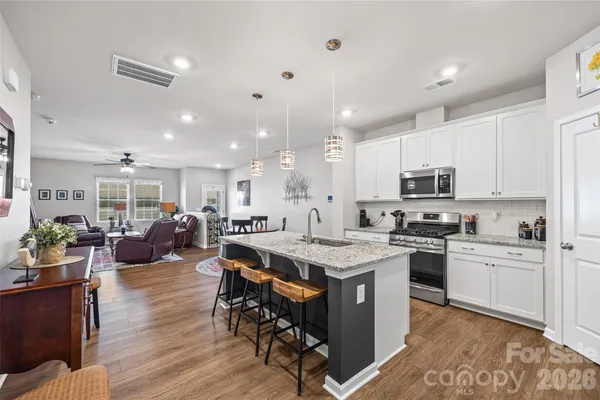 a kitchen with stainless steel appliances kitchen island granite countertop a stove a refrigerator a sink a dining table and chairs with wooden floor