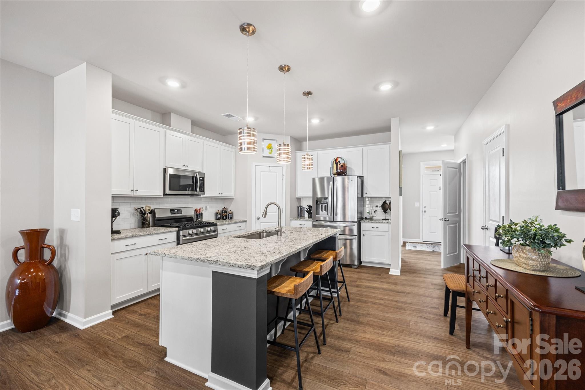 909 Cobbled Way Fort Mill, SC 29715 - Photo 6 of 31 a kitchen with stainless steel appliances kitchen island granite countertop a stove a refrigerator a sink a dining table and chairs with wooden floor