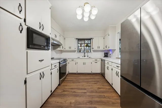 a kitchen with stainless steel appliances kitchen island granite countertop a refrigerator a sink dishwasher a stove and a dining table with wooden floor