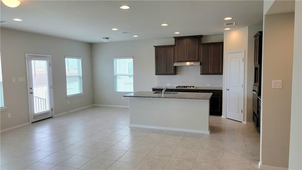 2741 Winding Creek Road Kyle, TX 78640 - Photo 3 of 11 Kitchen with light stone counters, recessed lighting, a kitchen island with sink, decorative backsplash, and dark wood finish cabinets