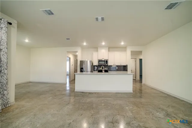 a view of a livingroom with kitchen appliances and a ceiling fan