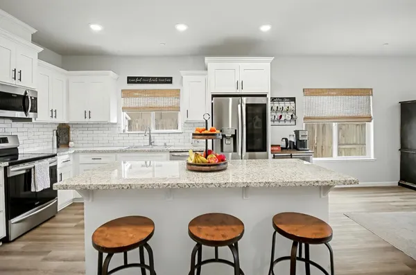 a kitchen with stainless steel appliances granite countertop a sink a stove a refrigerator and white cabinets with wooden floor