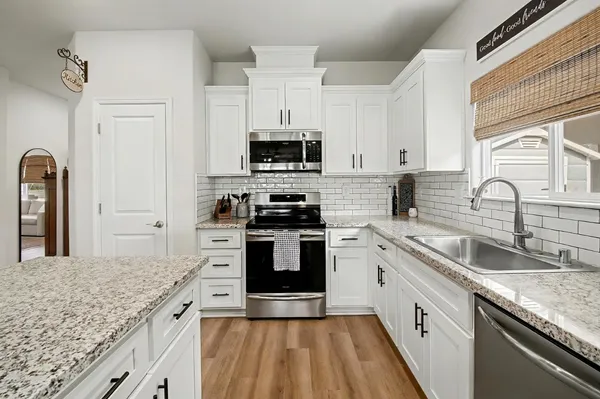 a kitchen with granite countertop a sink stainless steel appliances and white cabinets