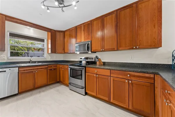 a kitchen with stainless steel appliances granite countertop wooden cabinets a sink a stove a refrigerator with grey cabinets and wooden floor