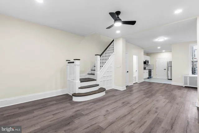 a view of an empty room with wooden floor and a ceiling fan