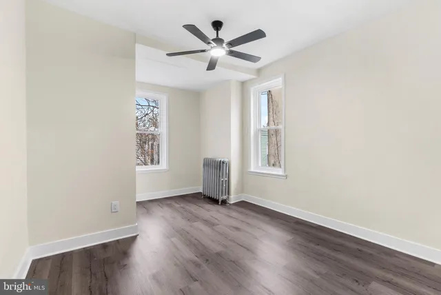 an empty room with wooden floor chandelier fan and windows