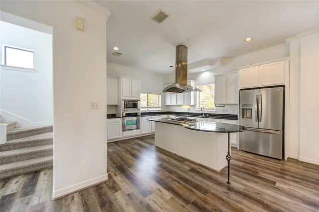 a kitchen with stainless steel appliances kitchen island hardwood floor sink and wooden cabinets