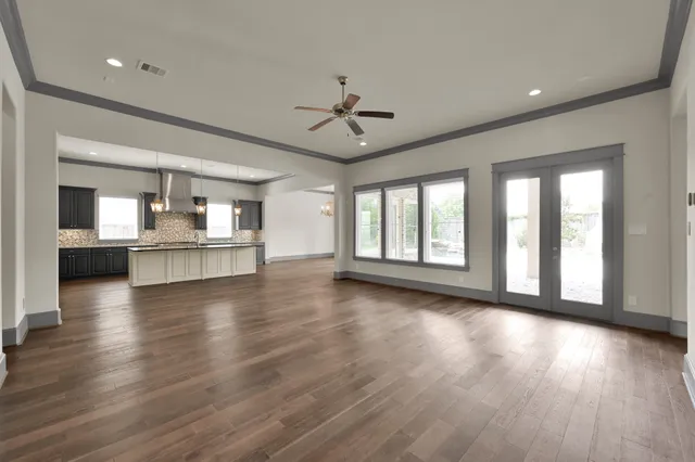 a view of an empty room with wooden floor and a kitchen