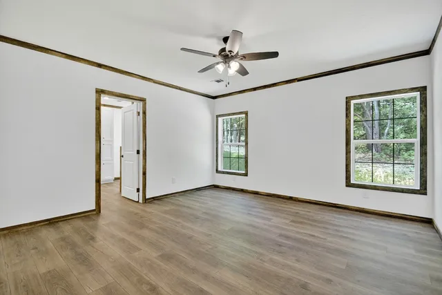 an empty room with wooden floor chandelier fan and windows