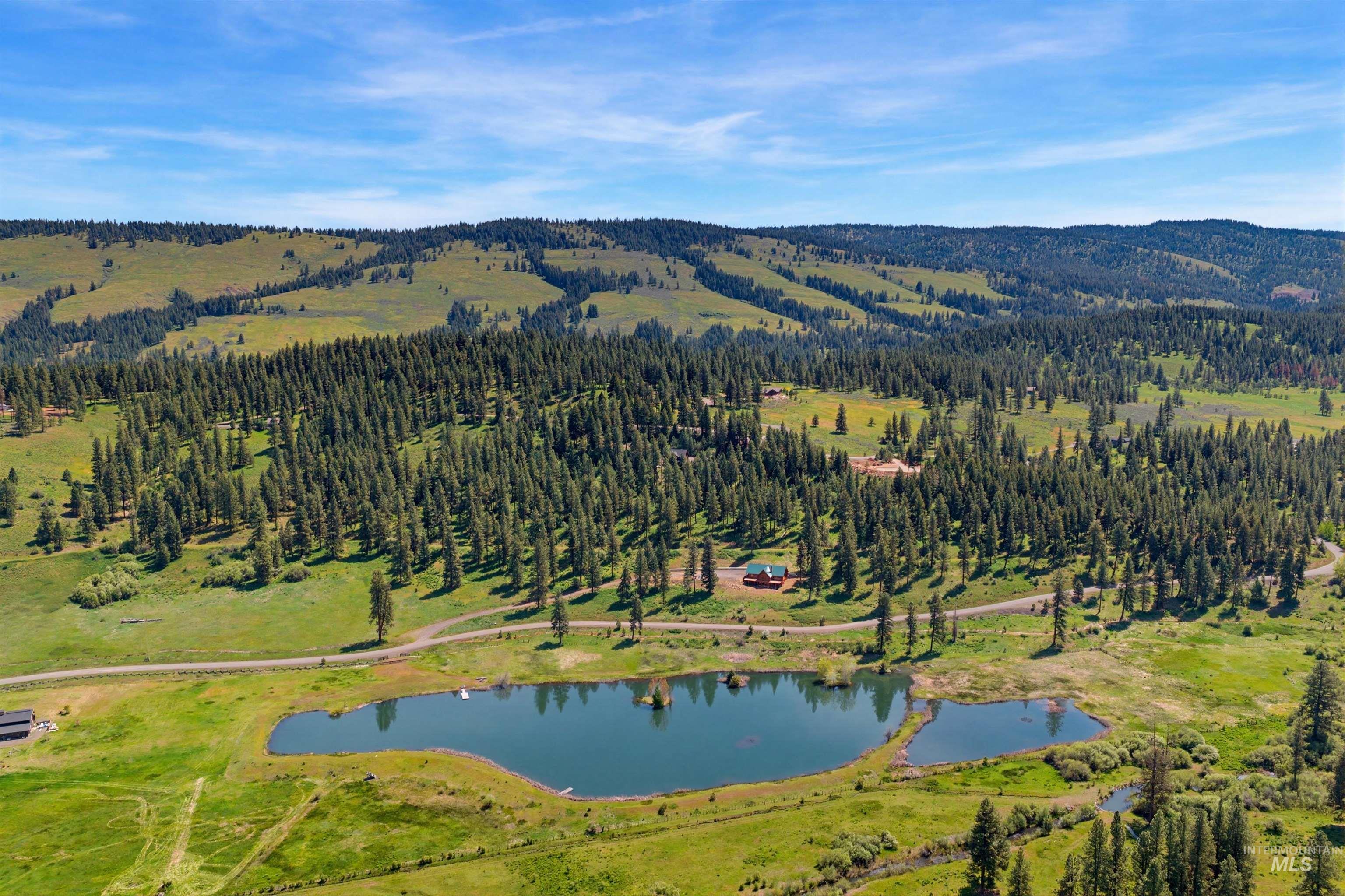 3322 Big Creek Road New Meadows, ID 83654 - Photo 1 of 50 Expansive rural landscape featuring a natural pond, a winding road, and a red-roofed building nestled among dense pine forests