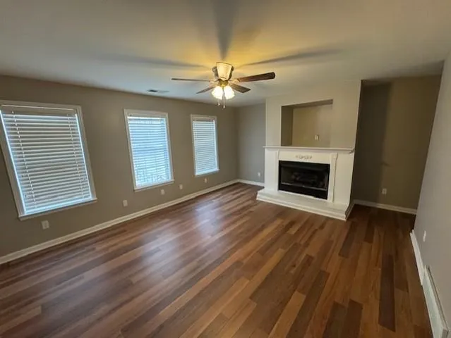 a view of an empty room with wooden floor fireplace and a window