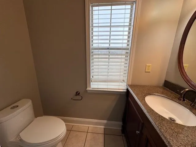 a bathroom with a granite countertop toilet a sink a mirror and a window