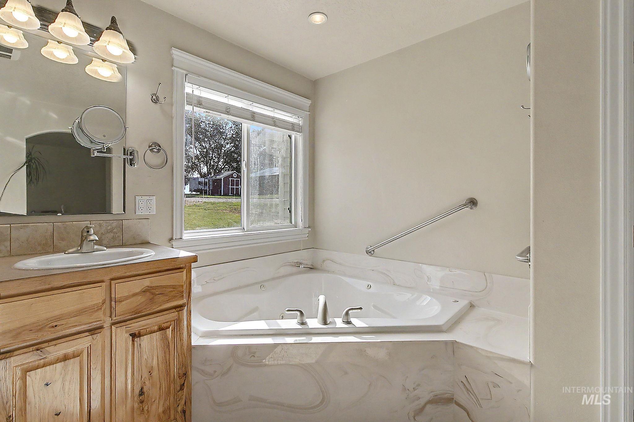 6900 West Charters Lane Melba, ID 83641 - Photo 32 of 49 Corner jetted tub with tiled surround, light wood-finish vanity, single basin sink, and an overhead vanity light fixture