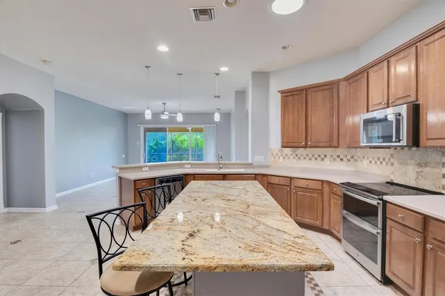 a kitchen with stainless steel appliances granite countertop a refrigerator a sink dishwasher a stove top oven and a dining table with wooden floor