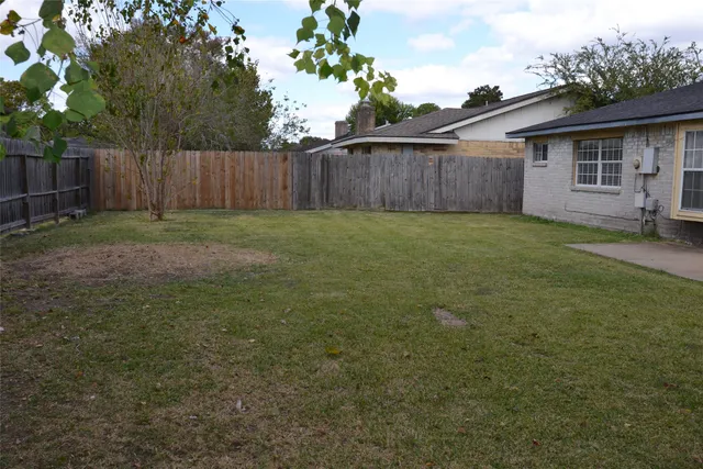 a view of a backyard with large trees and wooden fence