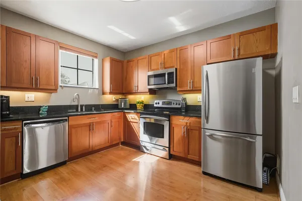 a kitchen with granite countertop wooden floors stainless steel appliances a sink and a window