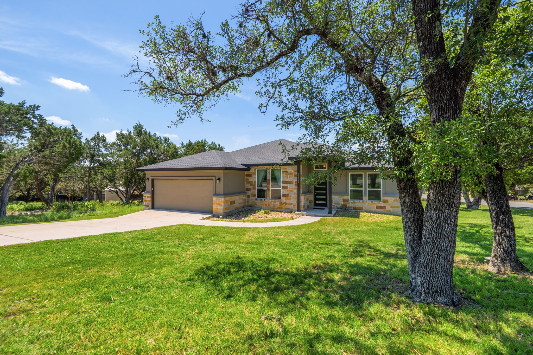 18605 Masters Cove Point Venture, TX 78645 - Photo 40 of 40 Contemporary single-story residence featuring a stone and stucco exterior, an attached two-car garage, a dark asphalt shingle roof, and a mature tree-lined front yard