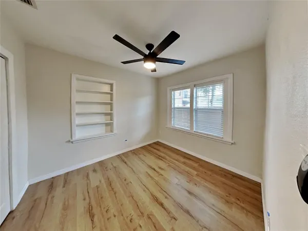 a view of empty room with wooden floor and fan