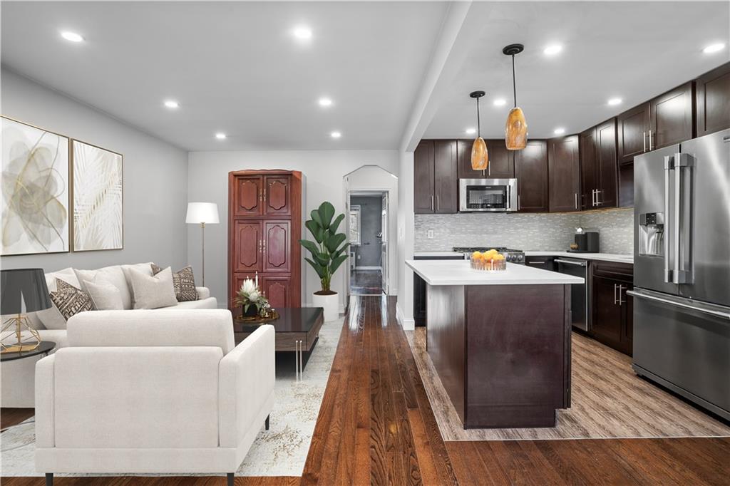 a living room with stainless steel appliances kitchen island granite countertop furniture a wooden floor and a large window