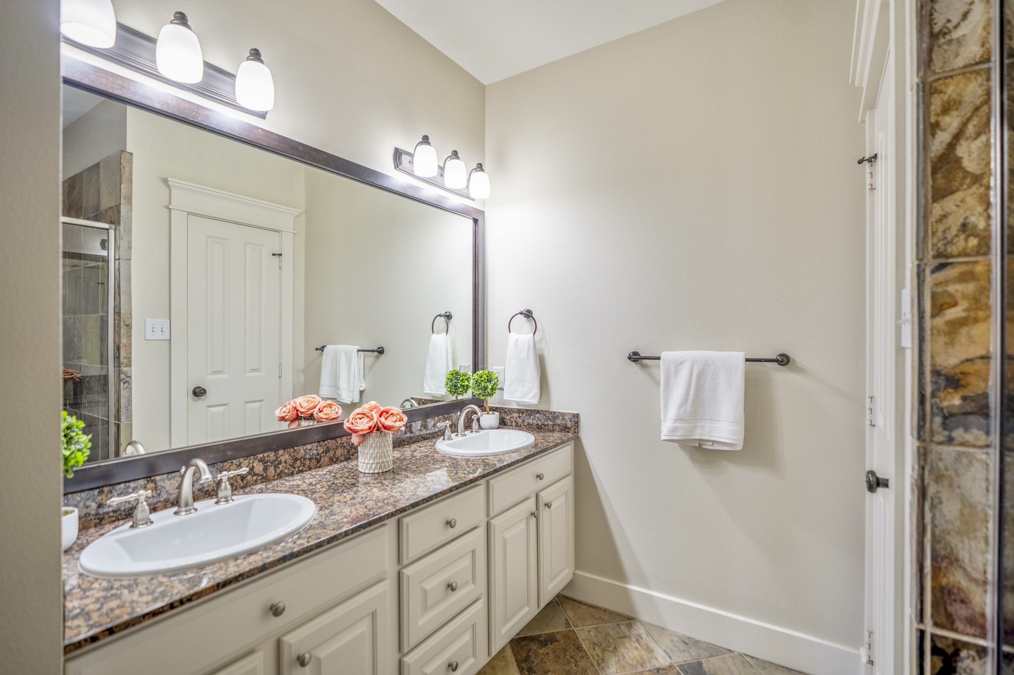 905 West 23rd Street Houston, TX 77008 - Photo 36 of 46 A well-lit bathroom features a double vanity with granite countertops and two sinks. The vanity is reflected in a large mirror above, which is illuminated by a row of lights.