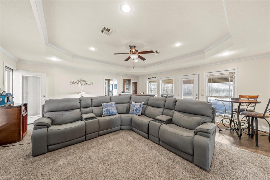 231 Trlica Road West, TX 76691 - Photo 23 of 36 This spacious second living area offers a comfortable and versatile layout ideal for relaxing or entertaining. A tray ceiling with crown molding and recessed lighting adds architectural detail, while a ceiling fan enhances comfort. The room features a built-in oak bar area with seating, creating a great space for gatherings, and large windows and glass doors bring in natural light and provide outdoor access. This inviting space works perfectly as a media room, game room, or casual family living room.