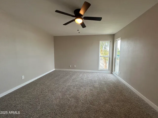 an empty room with ceiling fan and windows
