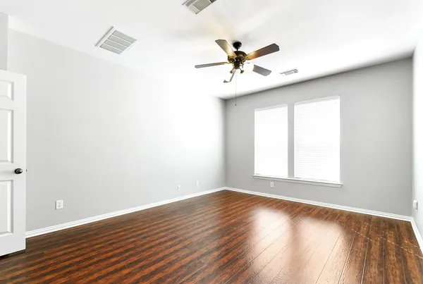 an empty room with wooden floor fan and windows