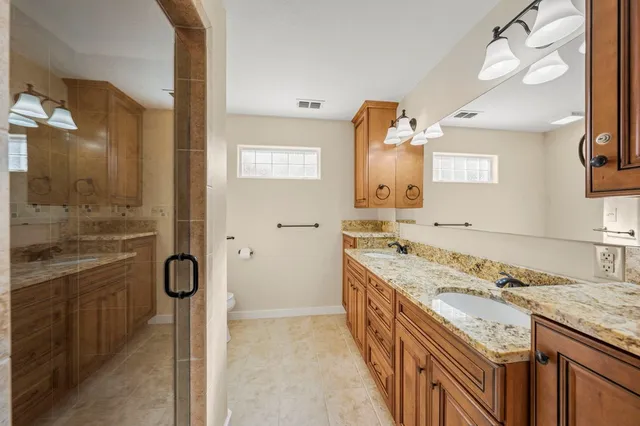 a spacious bathroom with a granite countertop double vanity sink a mirror and a shower