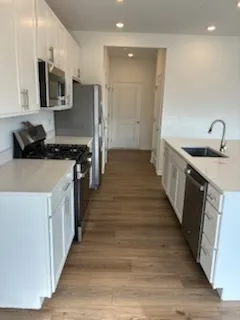 a kitchen with stainless steel appliances a stove top oven a sink a refrigerator white cabinets and wooden floor