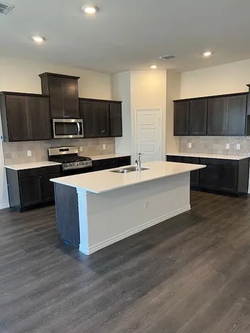 a large kitchen with stainless steel appliances wooden cabinets and a wooden floor