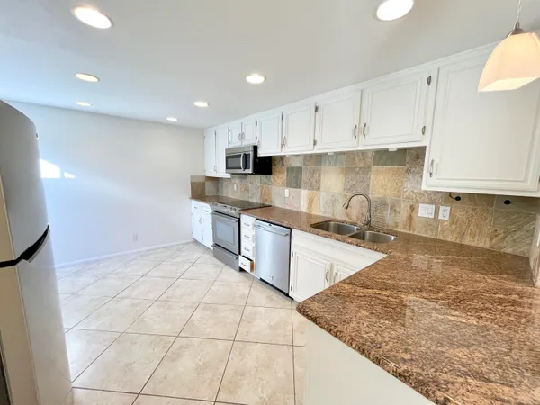 a large kitchen with granite countertop a stove a sink a counter space and cabinets