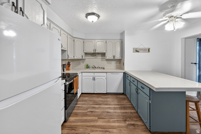 1218 East 100 South Logan, UT 84321 - Photo 7 of 23 Kitchen featuring wood-finish flooring, white cabinetry with dark hardware, a white refrigerator, and a ceiling fan