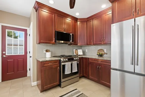 a kitchen with stainless steel appliances granite countertop a stove top oven a refrigerator and a sink with wooden cabinets