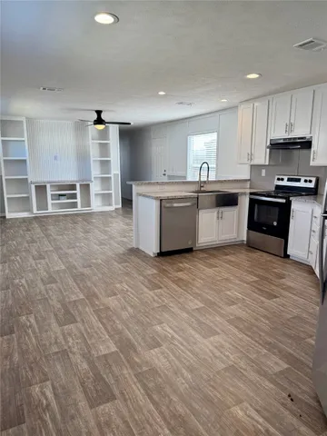 a large kitchen with stainless steel appliances granite countertop a large counter top a stove a sink and a refrigerator with wooden floor