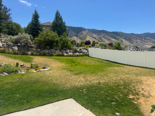 88 Canterbury Lane Logan, UT 84321 - Photo 35 of 37 Expansive terraced yard featuring a rock retaining wall, mature evergreen trees, a white vinyl fence, and distant mountain scenery