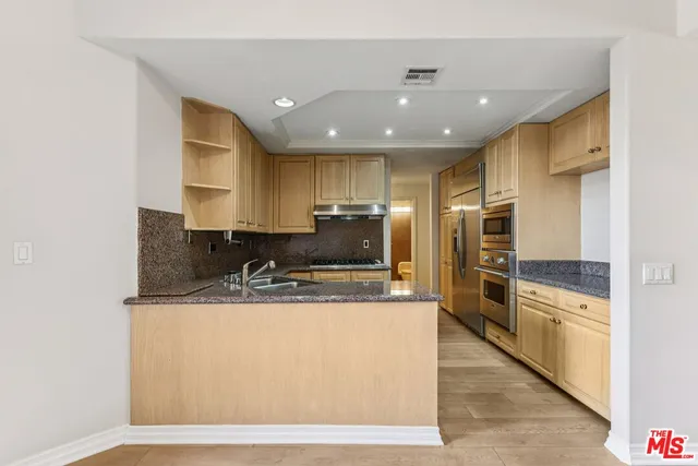 a kitchen with stainless steel appliances granite countertop a stove a refrigerator a kitchen island and chairs with wooden floor