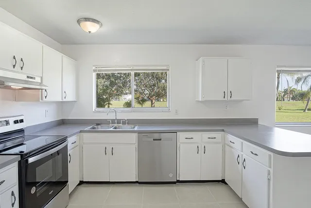 a kitchen with white cabinets appliances a sink and a window