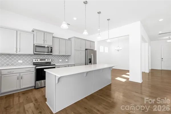 a kitchen with stainless steel appliances granite countertop a stove a sink a refrigerator and white cabinets with wooden floor