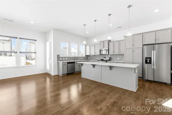 a kitchen with stainless steel appliances granite countertop a refrigerator a sink dishwasher a stove and white cabinets with wooden floor