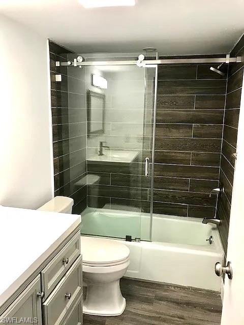 200 Valley Stream Drive, Unit 8B Naples, FL 34113 - Photo 12 of 15 Bathroom featuring a modern vanity with light grey cabinetry and a white countertop, wood-look floor tiles, a bathtub with a clear glass sliding door, and dark grey subway tiles in the shower