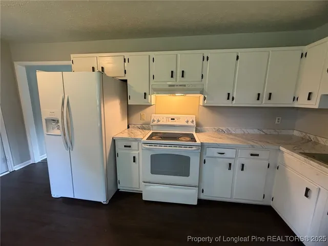 a kitchen with granite countertop white cabinets and refrigerator
