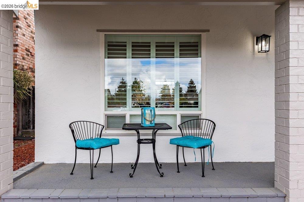 1298 Ribbon Street Foster City, CA 94404 - Photo 14 of 86 Covered porch featuring a window with interior shutters, textured stucco exterior, brick columns, an outdoor wall lantern, and a concrete patio surface